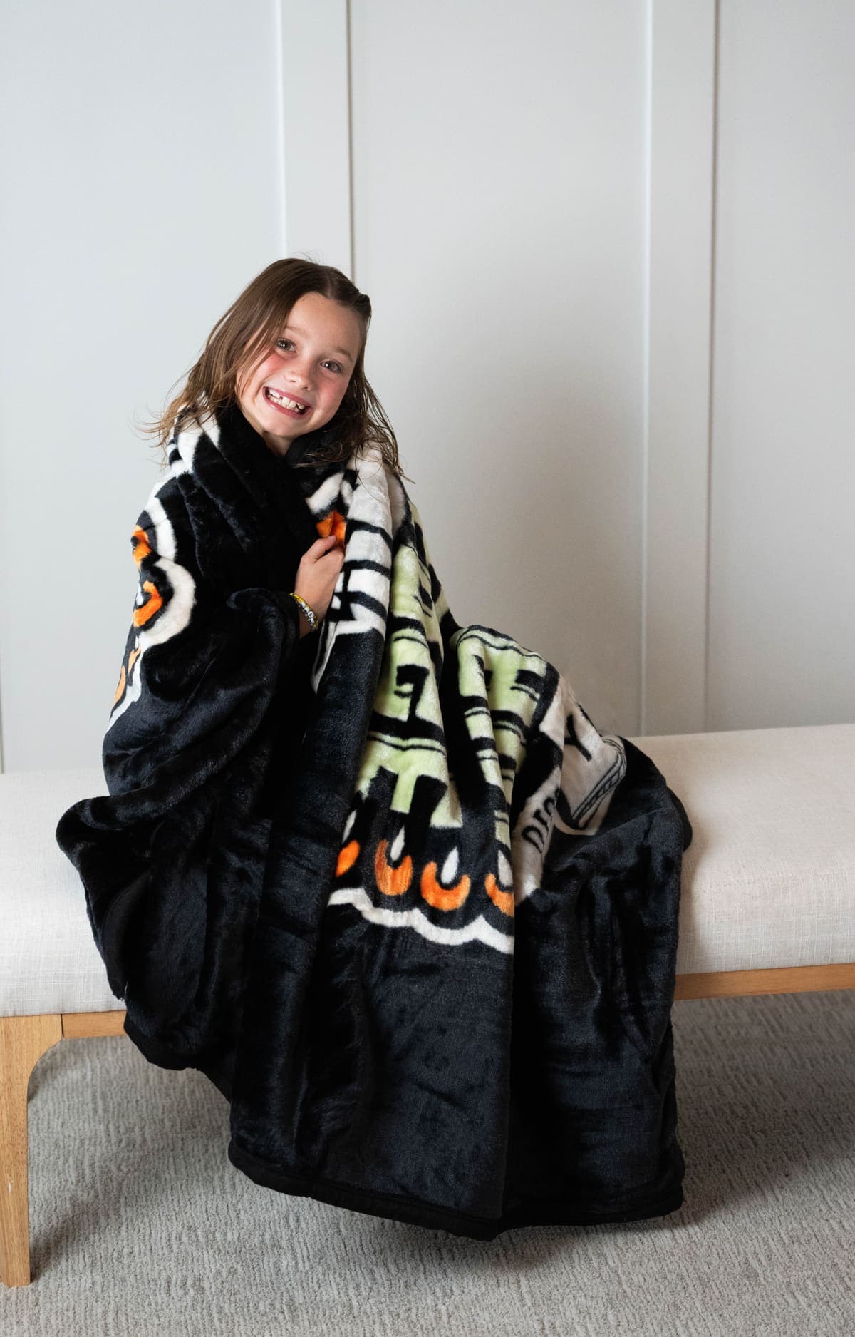 A young woman wrapped in the plush gray faux-fur Swanky Blanky, with the custom NubaySoft 2.0 school design showing on the front